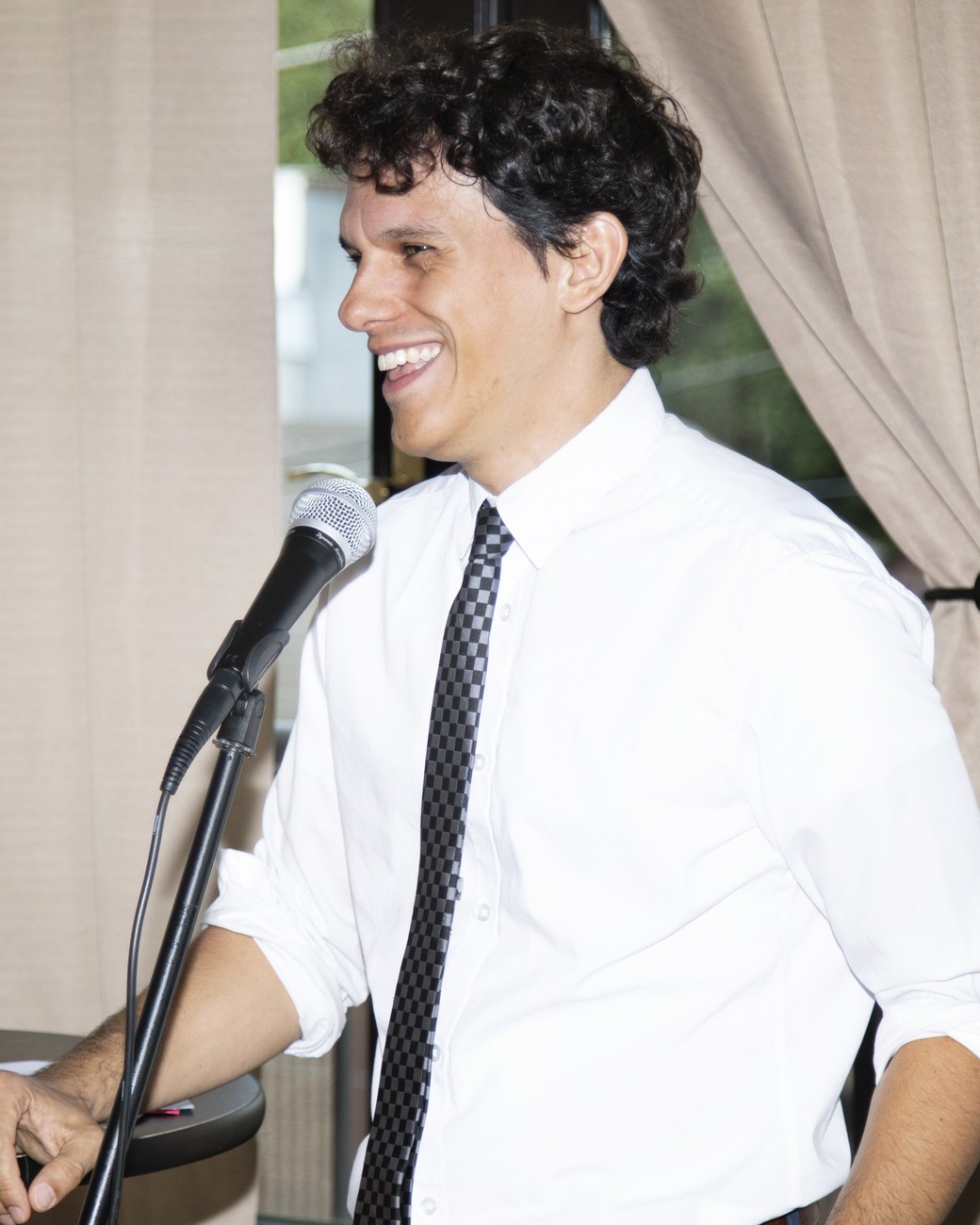 Andrés Cruciani speaking at a microphone, shirt and tie